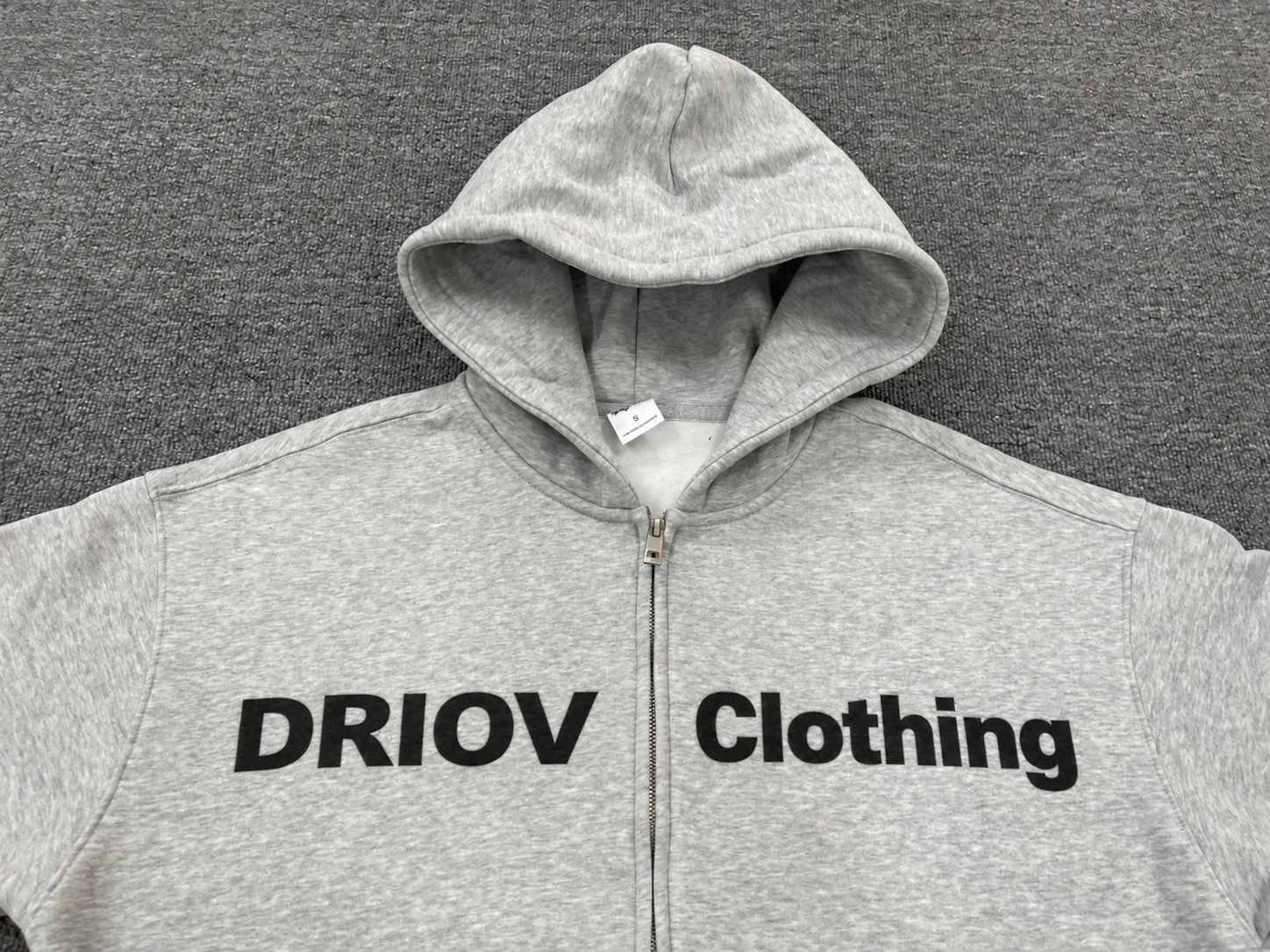 Black DRIOV Clothing lettering positioned on either side of a grey hoodie zipper.