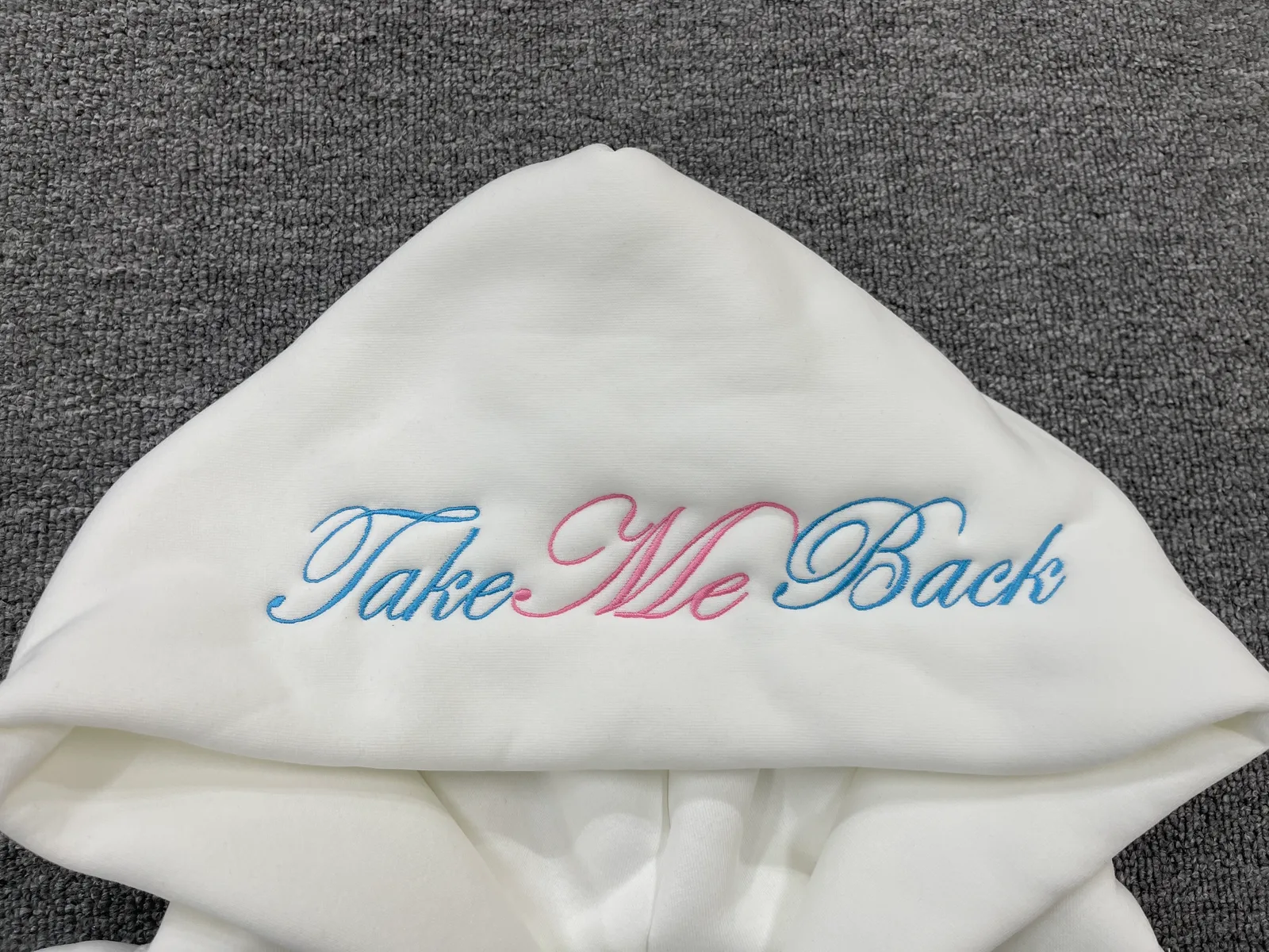 Blue and pink script embroidered across the hood of a white garment.