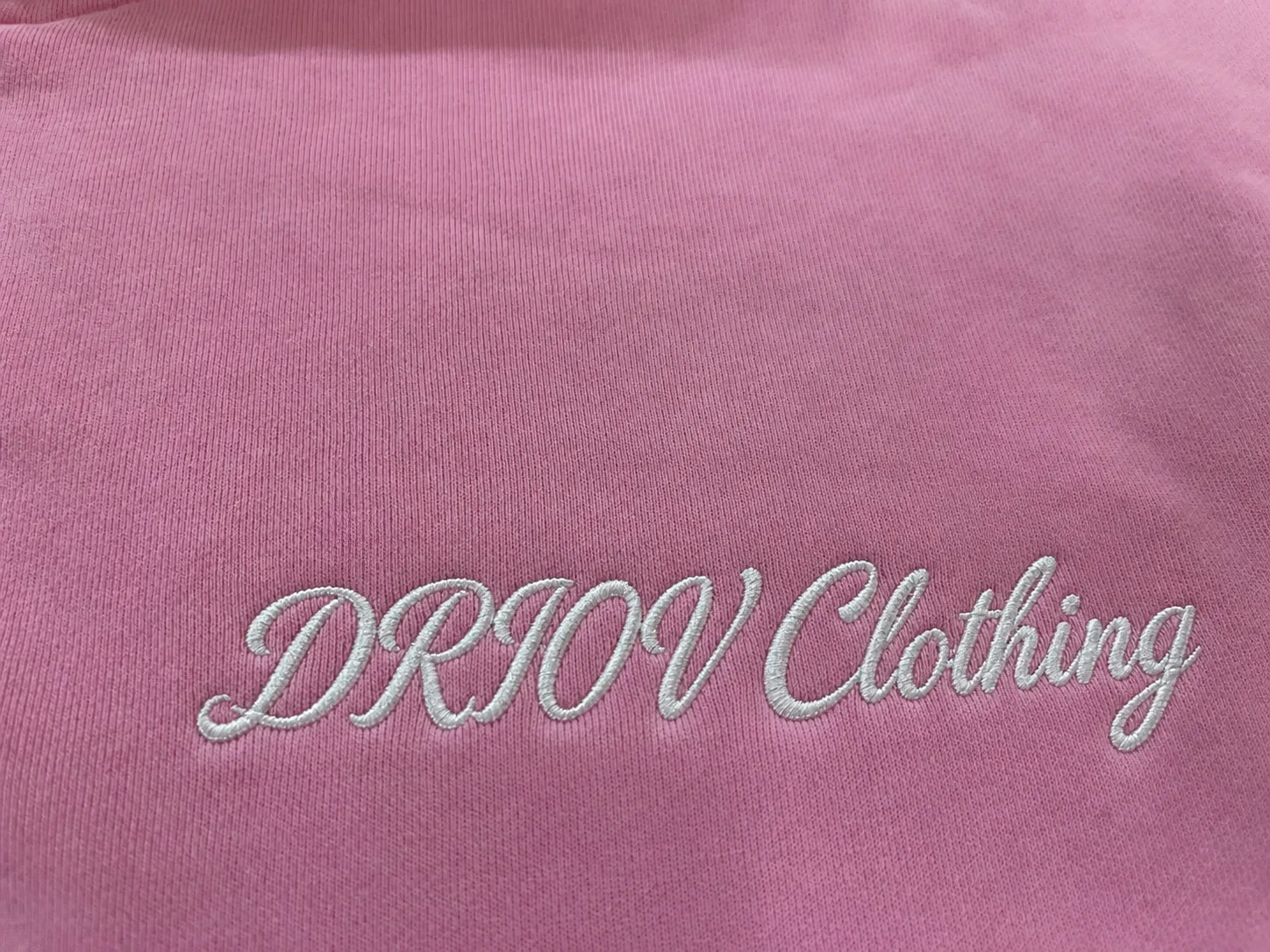 Light DRIOV Clothing script embroidery on pink fabric.