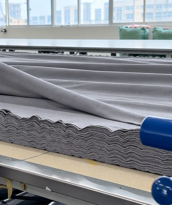 Layers of grey fabric spread on a cutting table.