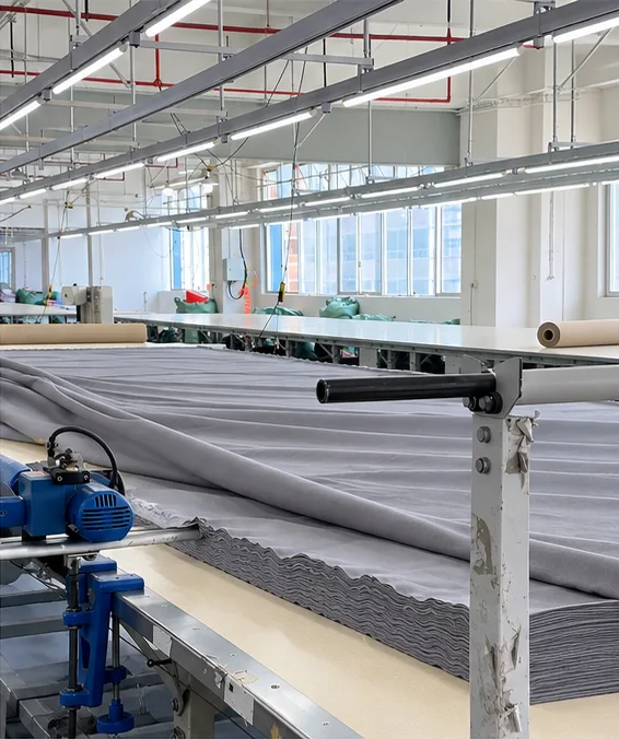 A cutting table with layers of grey fabric and cutting equipment.
