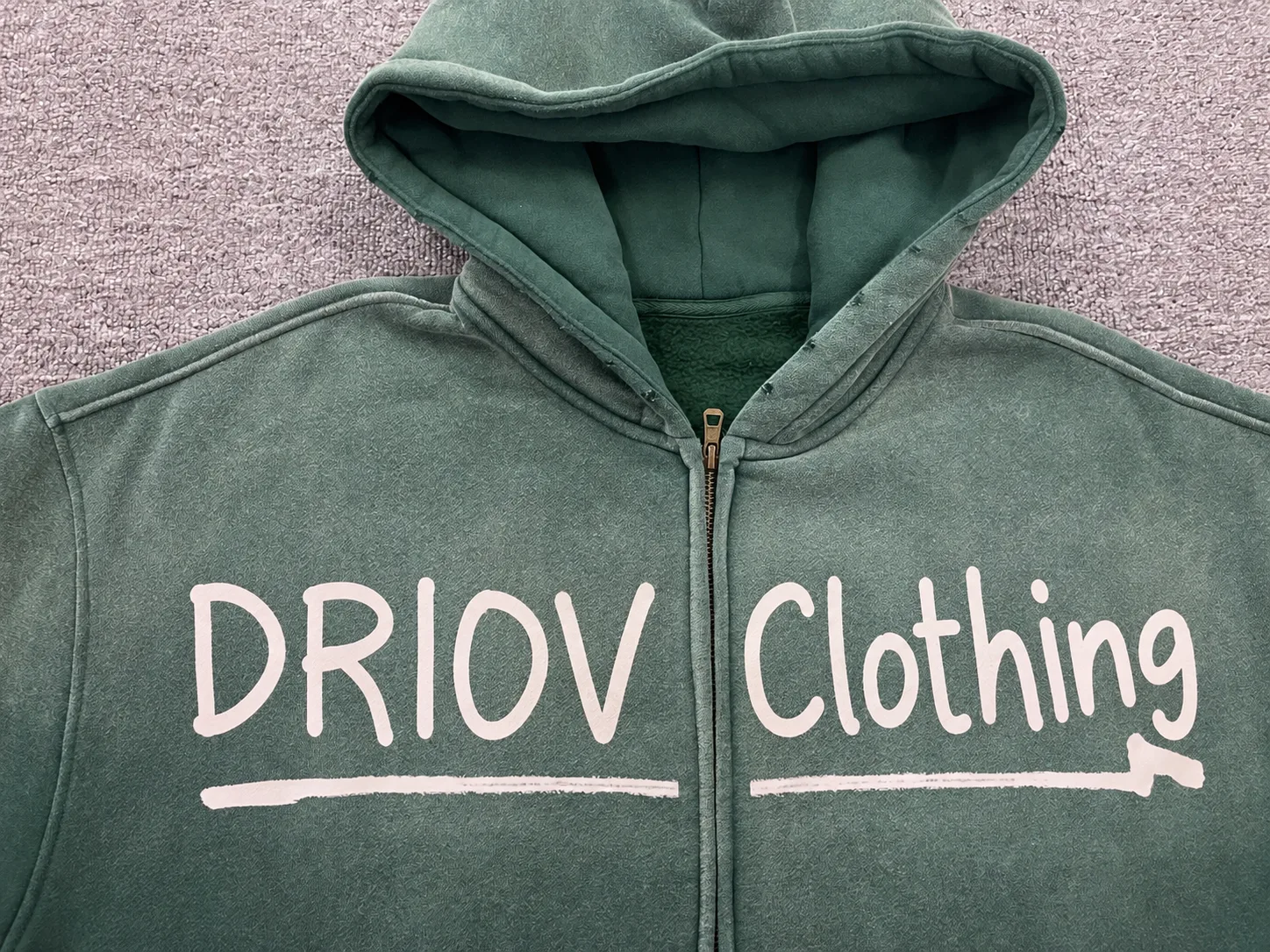 Light handwritten-style DRIOV Clothing lettering across a green zip hoodie.