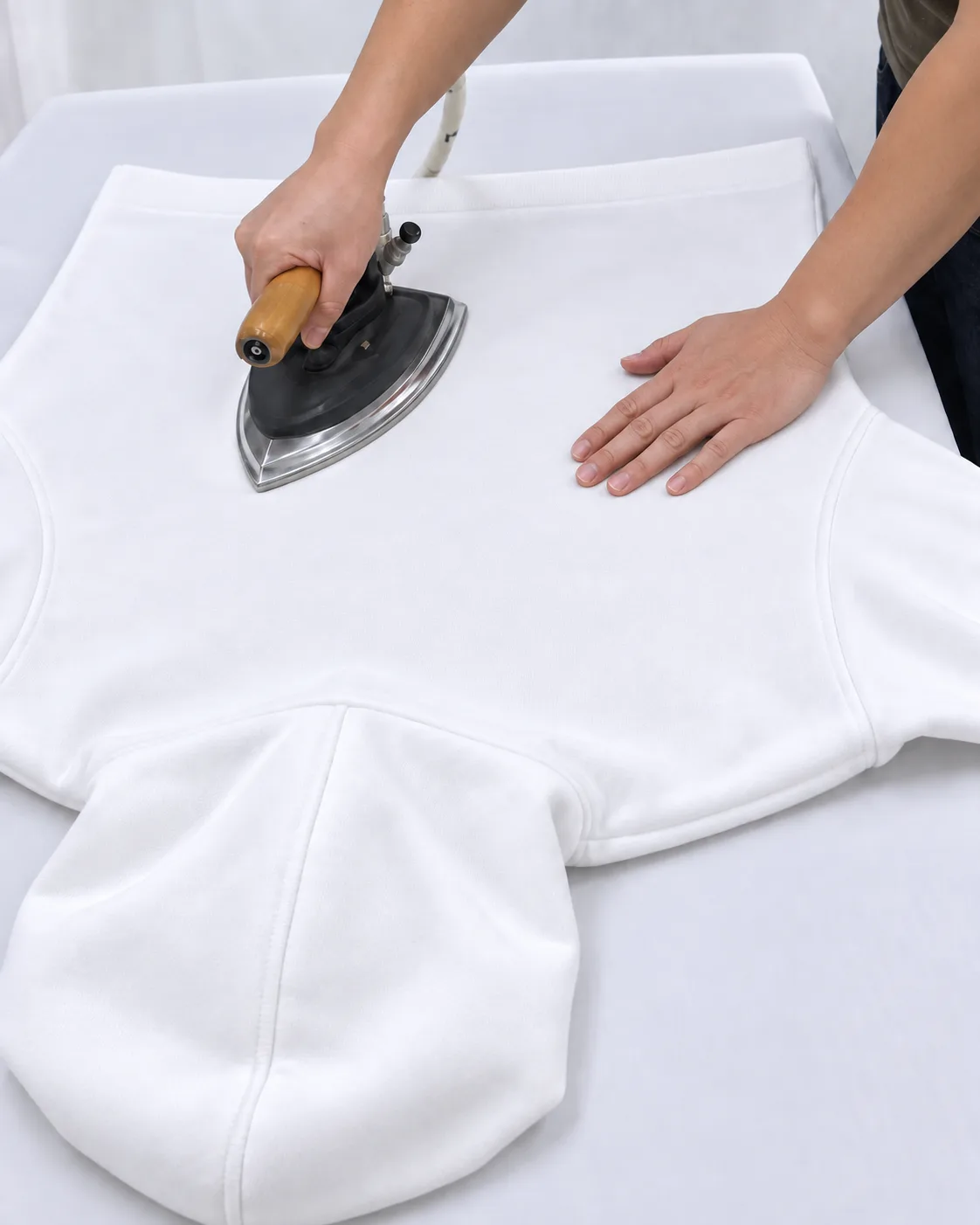 A white hoodie being pressed on a finishing table.