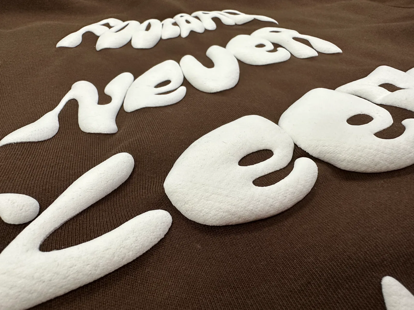 Close angled view of raised white rounded lettering on brown fabric.