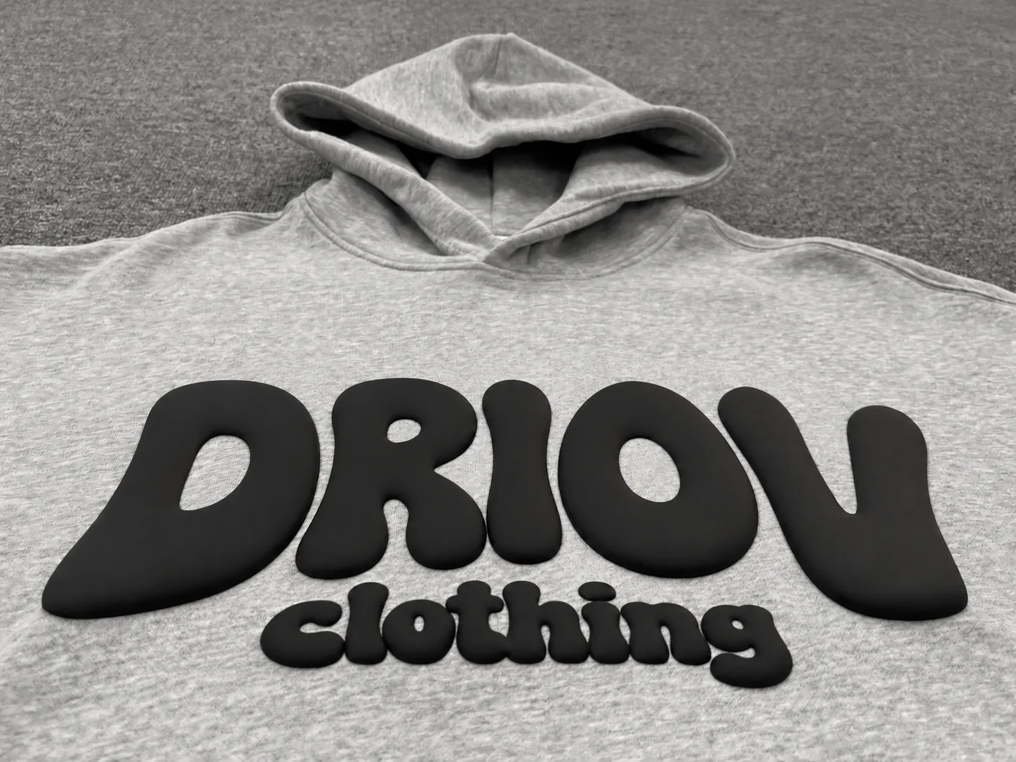 Rounded black DRIOV Clothing puff lettering across a grey hoodie.