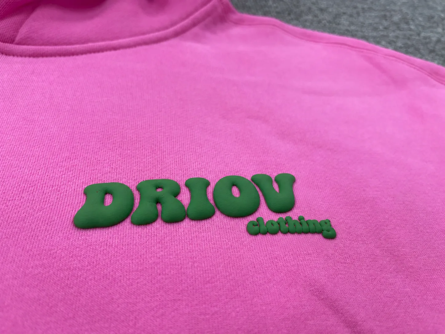 Green raised DRIOV Clothing lettering on a pink hoodie.
